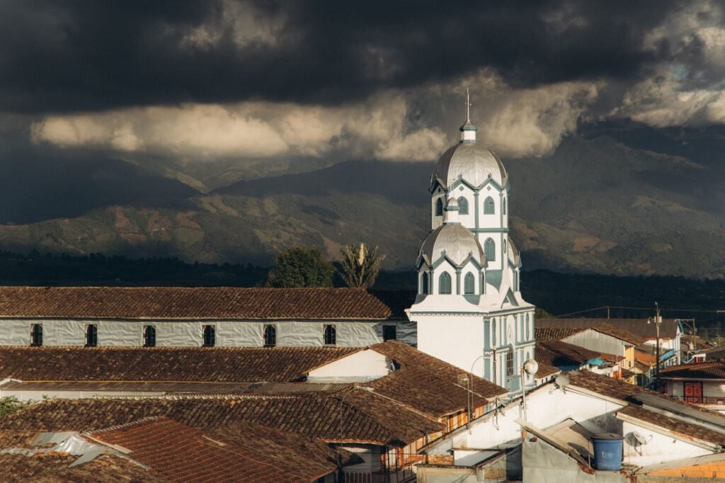Panoramic view of Iglesia Maria Inmaculada and rooftops against Quindio mountains under dramatic clouds., Quindío