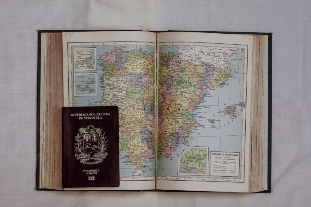 Open vintage atlas showing Spain and Portugal with a Venezuelan passport on top, symbolizing travel., Viajes a Colombia