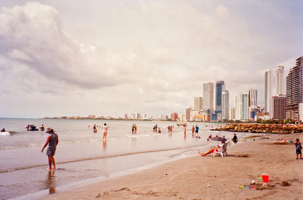 Beach scene with people enjoying Playa de Bocagrande in Cartagena, Colombia, featuring cloudy skies and a modern skyline., Cartagena