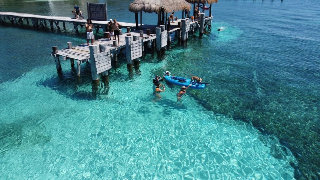 People enjoying a sunny day at Isla Mujeres pier with clear water and vibrant scenery., Islas de Rosario
