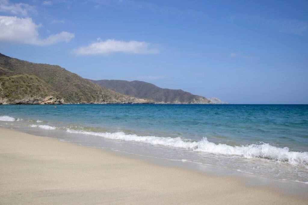 Serene sandy beach and turquoise ocean with lush mountains in Tayrona National Park., Tayrona