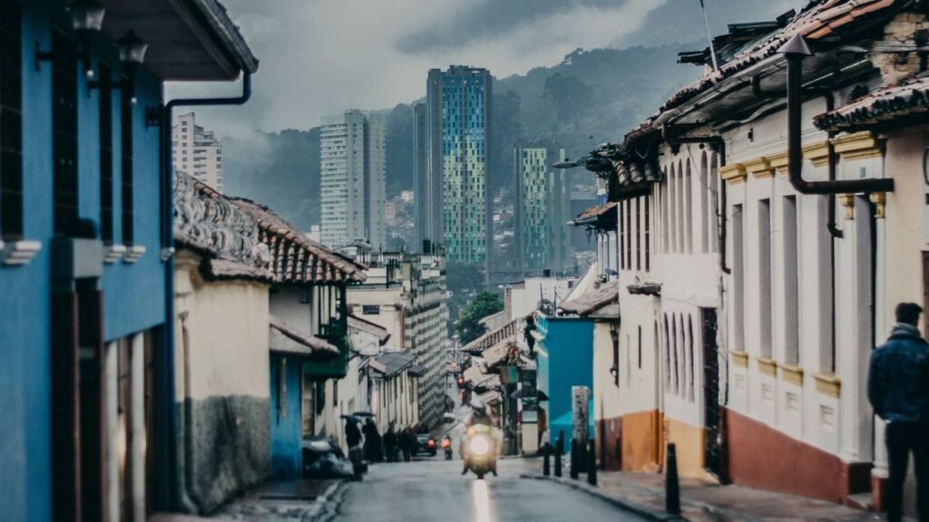Charming street scene in Bogotá with colorful houses and towering skyscrapers under cloudy skies.