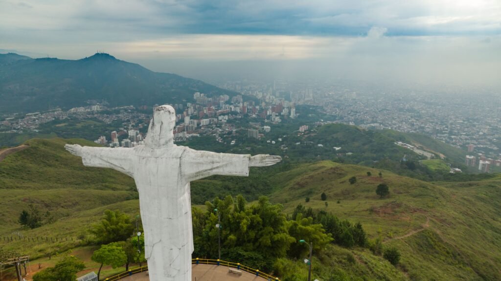 Aerial shot of Christ the Redeemer statue overlooking a cityscape and lush green hills. Colombia en 15 días