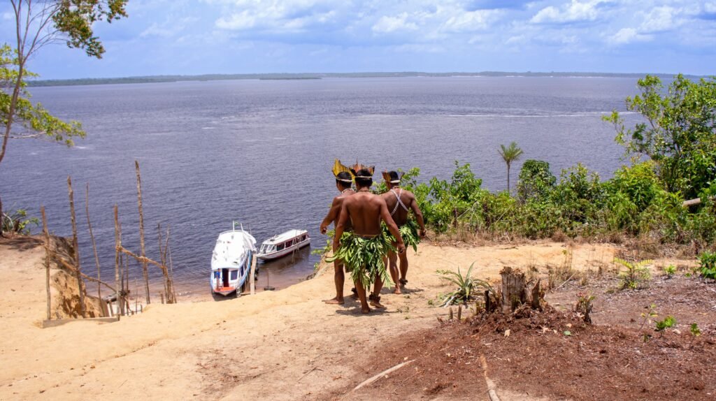 Indigenous men in traditional attire overlooking boats on the Amazon River. viaje al amazonas colombia
