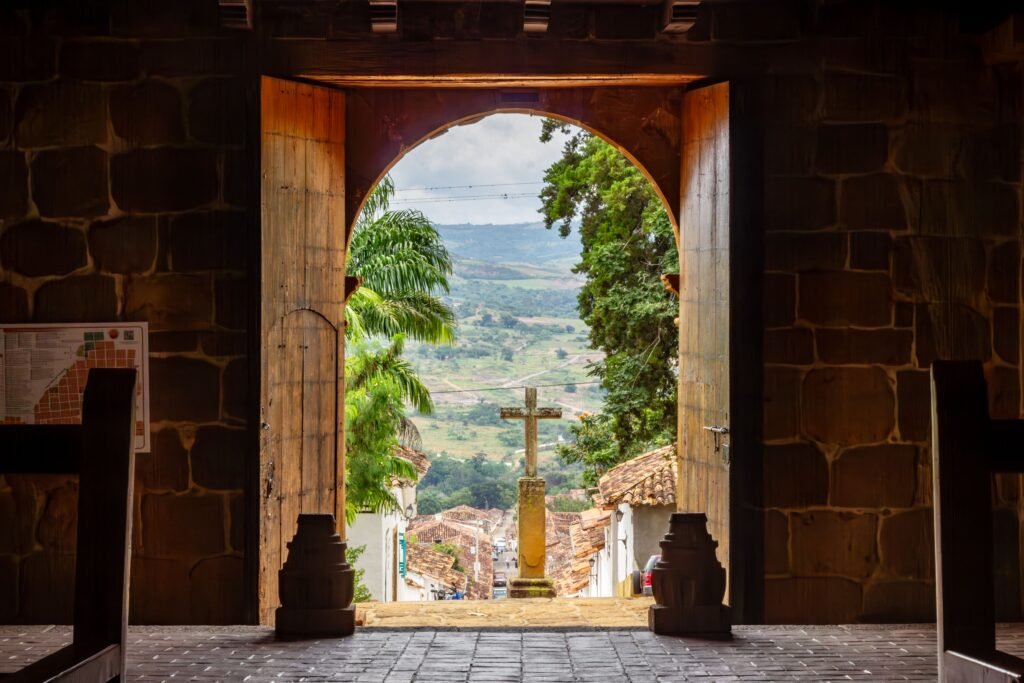 View through a church entrance in Barichara, Colombia, with a stone cross outdoors. Barichara