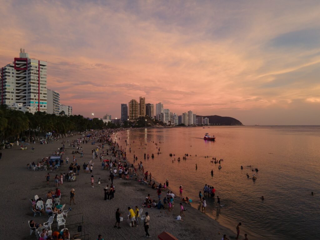 A bustling beach scene at sunset with a vibrant city skyline, capturing summer vibes and leisure. paquetes santa marta todo incluido