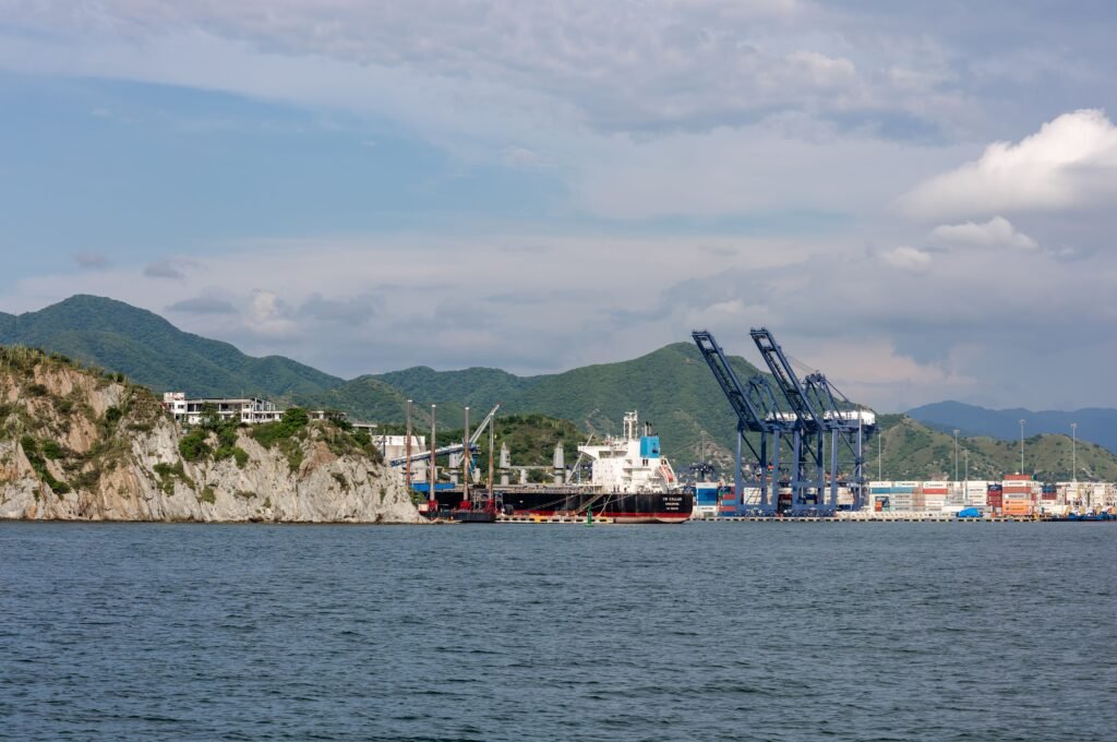 A vibrant coastal trading port with cranes, surrounded by sea cliffs and mountains under a bright sky. paquetes santa marta todo incluido