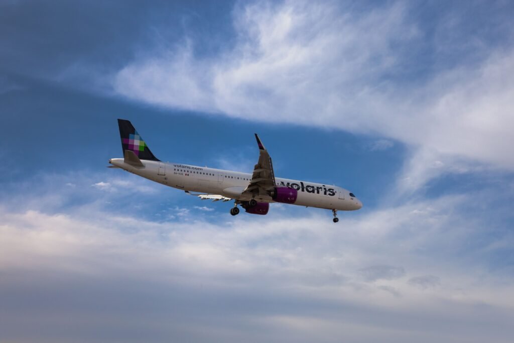 A commercial airplane flying against a vibrant blue sky with clouds. consejos para conseguir vuelos baratos