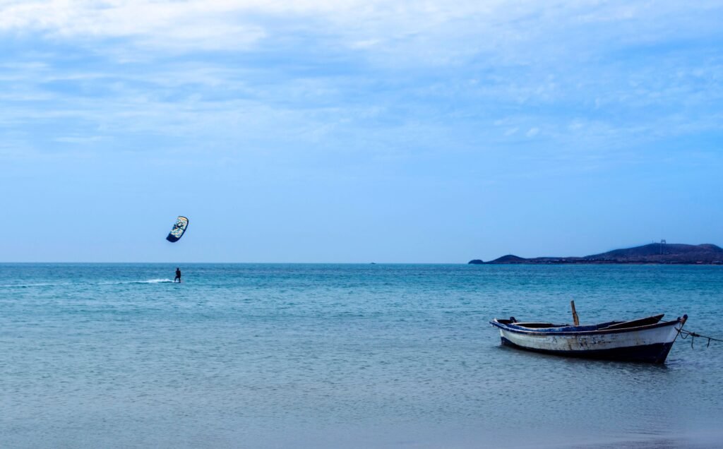 Amazing view of distant kite surfer practicing on blue sea near moored old boat in peaceful resort,  La Guajira